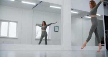 Jimnastikçi, beyaz salonun ayna duvarının önüne atlıyor. Beyaz salonda jimnastik, yoga ve pilates eğitmeni, 4k 120p Prores HQ.