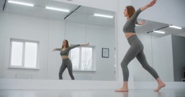 Dansçı kadın ayna duvarının önünde ağır çekimde atlıyor, beyaz dans salonunda jimnastik yapıyor, esneme antrenörü, yoga öğretmeni, 4k 120p Prores HQ