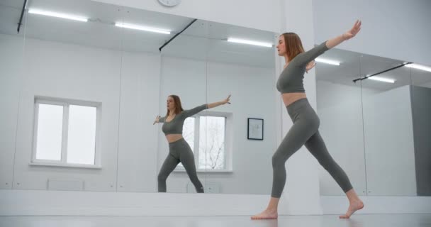 Dansçı kadın ayna duvarının önünde ağır çekimde atlıyor, beyaz dans salonunda jimnastik yapıyor, esneme antrenörü, yoga öğretmeni, 4k 120p Prores HQ — Stok video