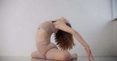 Yoga eğitmeni yerde ağır çekimde egzersiz yapar, bej kostümlü genç kadın pilates yapar ve beyaz arka planda egzersiz yapar, 4k 120p Prores karargahı.