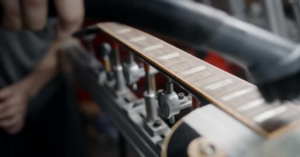 ギター技術は、スタンド、楽器の修理店、 4k 60fps 10ビットの後のギターネックから木材塵を除去するために掃除機を使用しています — ストック動画