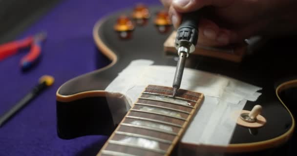 Geigenbauer erhitzt Bünde an der Gitarre durch Lötkolben vor dem Refrettieren, Vorbereitungen für Bündetausch in der E-Gitarre, 4k 60fps Prores HQ — Stockvideo