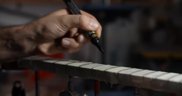 Gitarrenbauer markiert Bünde auf der Gitarre mit schwarzem Marker vor dem Schleifen, Musikinstrumentenwerkstatt, 4k 60p 10 bit — Stockvideo