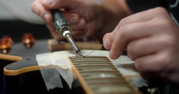 Luthier calienta trastes en la guitarra por soldador antes de volver a poner, preparaciones para el reemplazo de trastes en la guitarra eléctrica, 4k 60fps Prores HQ — Vídeo de stock