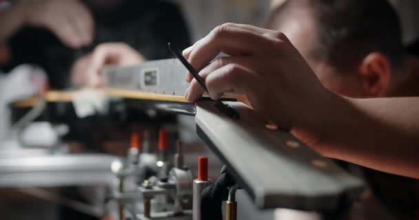 Luthier ajusta el ángulo del diapasón en la guitarra eléctrica montada en la plantilla, reparando los instrumentos musicales en hte shop, 4k 60p 10 bit — Vídeo de stock