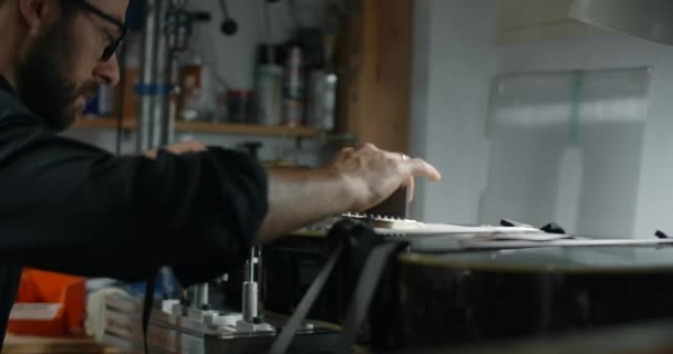 Luthier ajusta el ángulo del diapasón en la guitarra eléctrica montada en la plantilla, reparando los instrumentos musicales en hte shop, 4k 60p 10 bit — Vídeo de stock