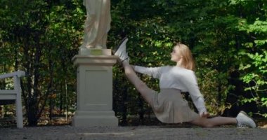 Genç dansçı kadın halka açık bir parkta sicimin üzerinde oturuyor. Açık havada esneme egzersizleri. Yaşam tarzı spor videoları açık havada, 4k 60 fps Prores Merkezi