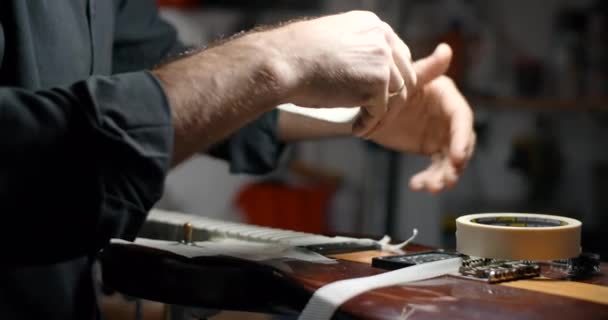 Ο Luthier καλύπτει το σώμα της κιθάρας με ταινία συγκάλυψης πριν τρίψει τα χαλίκια στο μαγαζί του. Φροντίδα και επισκευή των μουσικών οργάνων, 4k 60p Prores HQ — Αρχείο Βίντεο