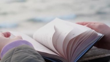 Rüzgar kitap sayfalarını yavaş çekimde çeviriyor. Açık kitap deniz kenarındaki bankta yatıyor, 4k 60 peni.