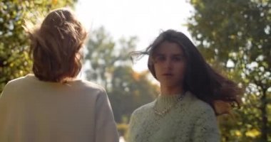Genç kadınlar güneş ışığıyla birlikte açık havada ağır çekimde yürüyorlar. Rastgele gezen iki kızın parkta 4k 60p Prores HQ 'daki moda videosu.
