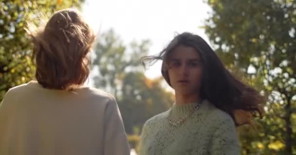 Genç kadınlar güneş ışığıyla birlikte açık havada ağır çekimde yürüyorlar. Rastgele gezen iki kızın parkta 4k 60p Prores HQ 'daki moda videosu. — Stok video