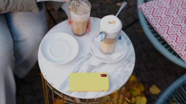 Sonbaharda eski kasabanın sokak kafesinde kaşık kaşık latte karıştırıyor, 4k 60 peni ağır çekim.