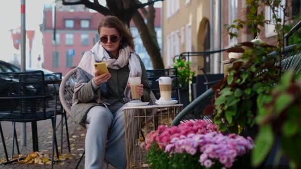 Donna turistica in occhiali da sole beve caffè caldo nel caffè di strada della città vecchia in autunno, 4k 60p rallentatore — Video Stock