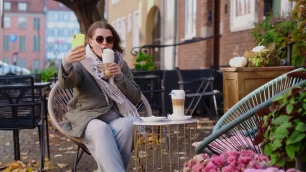 秋天，穿着太阳镜的博客和旅行女性在老城区的街头咖啡馆里自拍。咖啡店休息，4k60p慢动作 — 图库视频影像