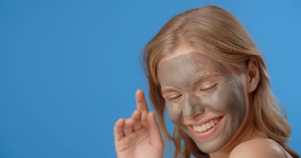 Uygulamalı kil maskeli mutlu kadın gülümsüyor. Kadınların kozmetik kullanımı. Mavi ekranda güzellik hizmetleri, 4k Prores Merkezi — Stok video