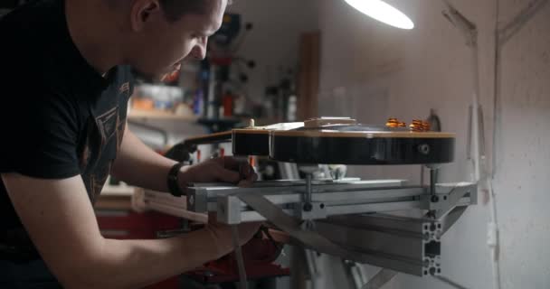 Guitar tech mounts the electric guitar on the jig at the musical instruments repairing shop, 4k 60p 10 bit — Stock Video