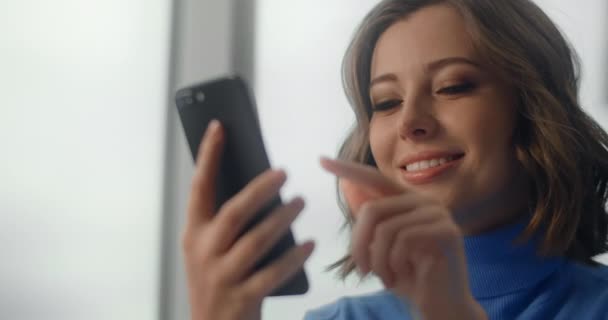 Молода європея махає екраном смартфона і посміхається в кабінеті, офісний працівник використовує телефон для соціальних мереж, 4k Prores HQ 10 біт — стокове відео
