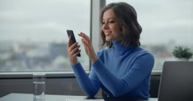 Genç Avrupalı kadın akıllı telefon ekranını araklıyor ve iş yerindeki dolabında gülümsüyor, ofis çalışanı sosyal medya için telefon kullanıyor, 4k Prores karargahı 10 bit