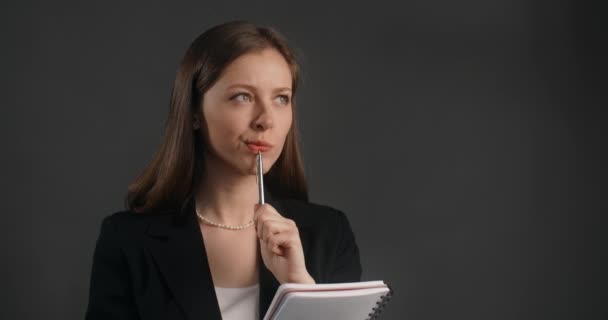 Jeune femme en costume noir pense un peu et écrit ses idées sur le bloc-notes en papier, en prenant les notes, 4k Prores HQ — Video