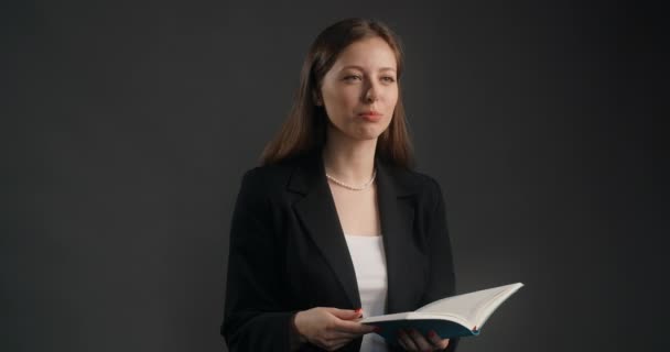 Jeune femme en costume noir écoute le interlocuteur avec le sourire et feuillette les pages de son bloc-notes, en prenant enquête, faire une entrevue, 4k Prores HQ — Video