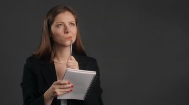 Young woman in black suit smiles and writes her ideas to the paper notepad, making the notes with happy look, 4k Prores HQ