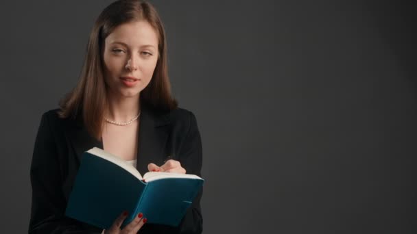 Jonge vrouw in zwart pak luistert naar de collocutor met een glimlach en maakt notities aan het papier notitieblok, het nemen van onderzoek, het maken van interview, 4k Prores HQ — Stockvideo