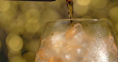 MACRO SHOT of the pouring alcohol to the cocktail glass full of ice cubes, brandy is poured to the glass, 4k 120fps Prores HQ