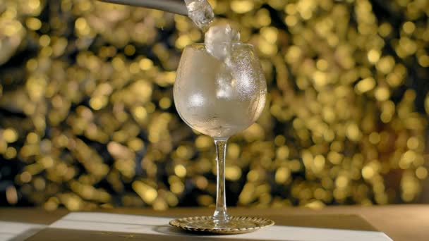 Ice cubes are being dropped to the cocktail glass in slow motion on the golden sparkle background, Full HD Prores HQ 240 fps — Stockvideo