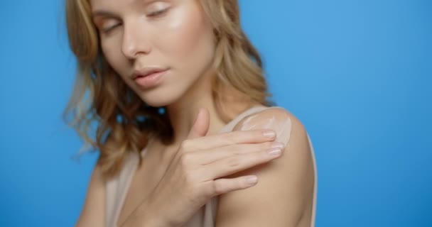 Blonde pretty woman applies body mask to her shoulder in slow motion. Womens cosmetics usage. Beauty care procedures on blue screen, 4k Prores HQ — Wideo stockowe
