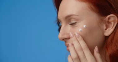 Portrait of pretty woman applying cream to her face. Womens cosmetics usage. Beauty care procedures on blue screen, 4k Prores HQ