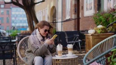 Traveller woman in sunglasses does does photos of her coffe cups by smartphone in the street cafe of old town, 4k 60p slow motion