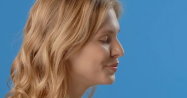 Blonde woman sprays micellar water to her face. Womens cosmetics usage. Beauty care procedures on blue screen, 4k Prores HQ