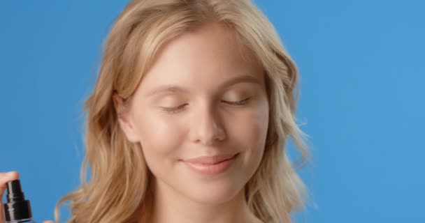 Blonde woman sprays micellar water to her face. Womens cosmetics usage. Beauty care procedures on blue screen, 4k Prores HQ — 비디오