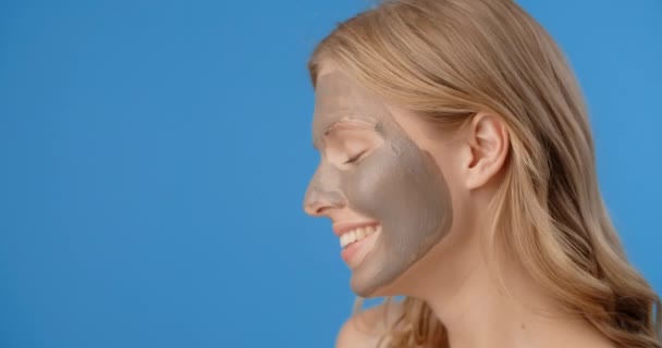 Szczęśliwa kobieta uśmiecha się w glinianej masce. Wykorzystanie kosmetyków dla kobiet. Pielęgnacja urody na niebieskim ekranie, 4k Prores HQ — Wideo stockowe