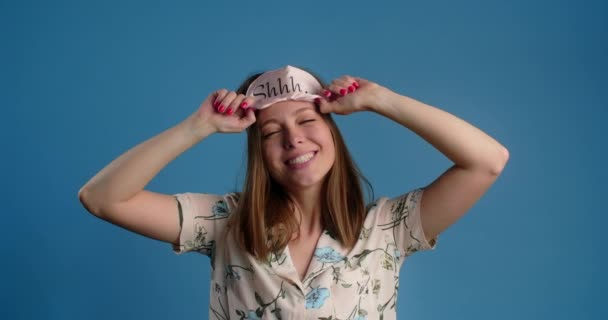 Portrait of a young woman who takes off her sleeping mask and smiles on the blue background, 4k 60p Prores HQ — Vídeo de Stock