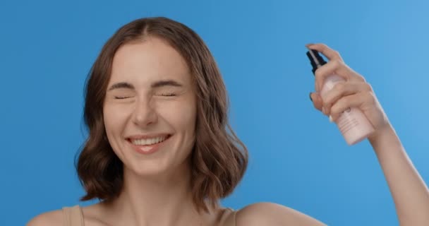 Woman sprays hair mask to her head. Womens cosmetics usage. Beauty care procedures on blue screen, 4k Prores HQ — Stockvideo