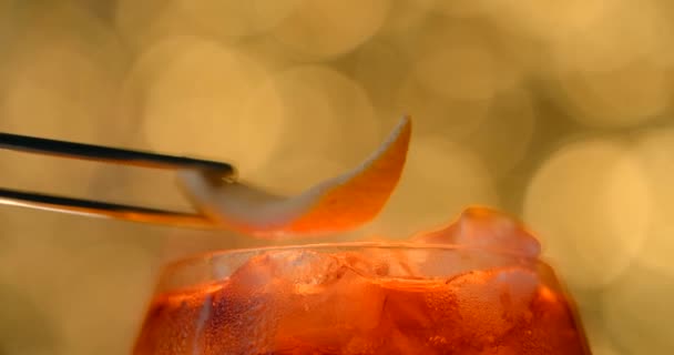 Oranges zest is added by tweezers to the cocktail glass full of ice. Making of the alcohol cocktail. 4k 120 fps Prores HQ — Video