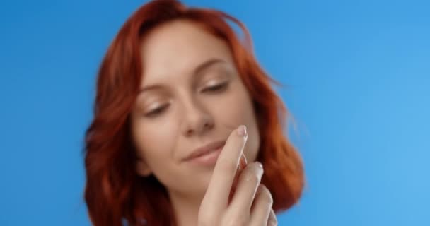 Redhead pretty woman applies skincare cream to her hands. Womens cosmetics usage. Beauty care procedures on blue screen, 4k Prores HQ — стоковое видео