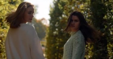 Genç kadınlar güneş ışığıyla birlikte açık havada ağır çekimde yürüyorlar. Rastgele gezen iki kızın parkta 4k 60p Prores HQ 'daki moda videosu.