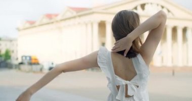 360 camera shot: young dancer in white dress dances on the stairs of the theatre in slow motion, balerina does dance steps and pa outdoors, 4k 120 fps Prores HQ