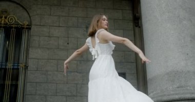 Young dancer in white dress dances on the stairs of the theatre in slow motion, balerina does dance steps and pa outdoors, 4k 120 fps Prores HQ