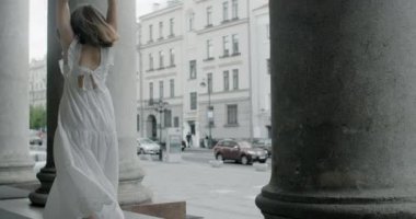 Young balerina in white dress dances on the stairs of the theatre in slow motion, balerina does dance steps and pa outdoors, 4k 120 fps Prores HQ