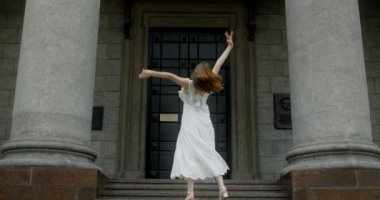 Young dancer in white dress dances on the stairs of the theatre in slow motion, balerina does dance steps and pa outdoors, 4k 120 fps Prores HQ