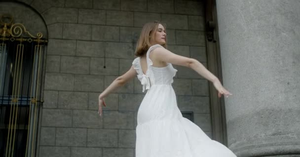 Young dancer in white dress dances on the stairs of the theatre in slow motion, balerina does dance steps and pa outdoors, 4k 120 fps Prores HQ — Vídeos de Stock