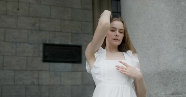Young dancer in white dress dances on the stairs of the theatre in slow motion, balerina does dance steps and pa outdoors, 4k 120 fps Prores HQ — Vídeos de Stock