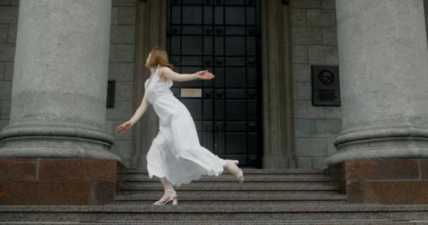 Young dancer in white dress dances on the stairs of the theatre in slow motion, balerina does dance steps and pa outdoors, 4k 120 fps Prores HQ — Vídeos de Stock