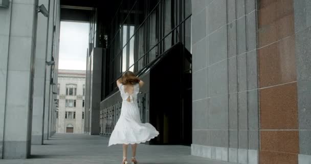 Young balerina in white dress whirls in the gallery of columns architectural complex in slow motion, balerina dances outdoors, 4k 120 fps Prores HQ — Stok video