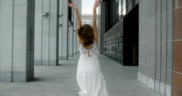 Young balerina in white dress runs through the gallery of columns in architectural complex in slow motion, balerina dances outdoors, 4k 120 fps Prores HQ — Stock video