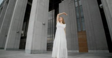 Young dancer in white dress dances in the gallery of columns architectural complex in slow motion, balerina does dance steps and pa outdoors, 4k 120 fps Prores HQ