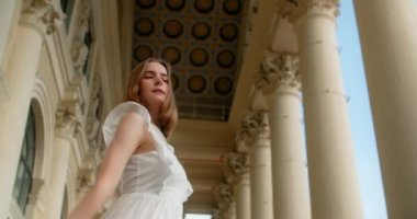 Young dancer in white dress dances on the stairs of the theatre in slow motion, balerina does dance steps and pa outdoors, 4k 120 fps Prores HQ